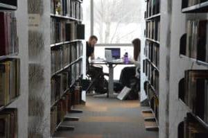 女学生和男学生在图书馆的书架之间的桌子上学习